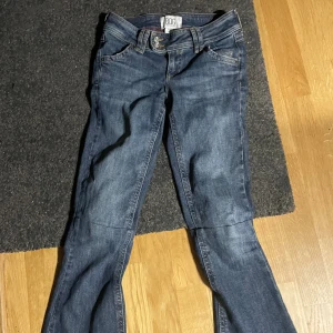Blå lågmidjade bootcut jeans från BDG - Snygga blå bootcut jeans från BDG med klassisk femficksdesign och normal passform. Jeansen har en mörk tvätt. Tillverkade i jeansmaterial med knapp- och dragkedjegylf. De är uppsydda vid knäet som inte syns på utsidan och är sytt vid knäet för att inte bootcut modellen ska förstöras, enkelt att sprätta up om man vill! 72cm innerben som de är nu ca 74 utan att de är uppsydda! W24 L34 använda ca 3 ggn
