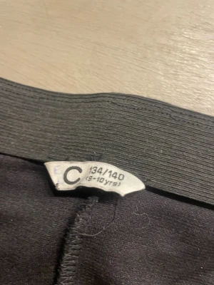 Svart shapewear kjol - Svart shapewear kjol med ribbad struktur och hög midja. Sitter tajt och formar midjan. Perfekt under kläder för en slätare siluett. Märkning för ålder 9-10 år. Materialet är stretchigt och bekvämt.