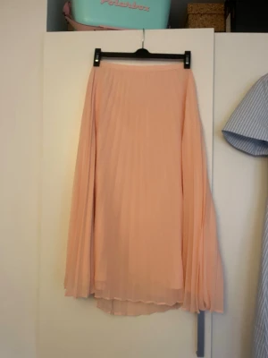 Ljusrosa plisserad långkjol - En ljusrosa långkjol med plisserat tyg från Gina Tricot. Den är i storlek 38.