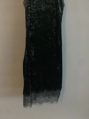 Svart sammetsklänning med spetskant - Mörk, svart klänning i mjuk sammet med spetsdetalj längst ner. Rak passform och ärmlös design ger en stilren look. Perfekt för dig som gillar en elegant och enkel stil med en twist av spets.