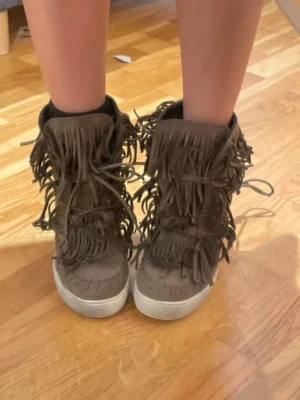 Bruna boots med fransar i mocka, Isabel marant liknande  - Säljer ett par bruna boots med massor av fransar och snörning framtill. Skorna är i mjuk mocka och har en platt sula. Perfekta för dig som vill sticka ut med din stil!