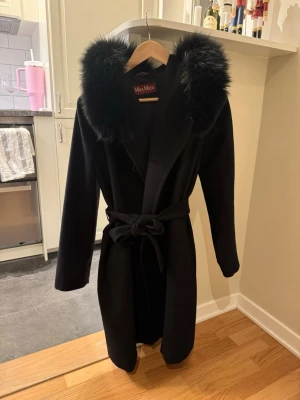 Max mara mango  - Max Mara Mango kappa Storlek XS Svart  I gott skick och har mycket mer att ge! Den har lite defekter så som skav vid ena fickan, samt på bältet (se bilder) - detta kan en skräddare enkelt fixa. Vilket har tagits med i beräkningen av priset. I övrigt är den fin!  Jag har även bytt ut hällorna i sidorna för bältet, då de tidigare släppte och var väldigt sköra. 