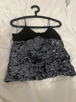 Svart paljettopp med spetsdetaljer - Säljer en topp med tunna axelband och glittriga silver paljetter. 