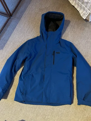 Skidjacka från Helly Hansen  - Säljer en skidjacka med en snygg blå färg från Helly Hansen. Den håller dig både torr och varm under skidåkning, dessutom är den väldigt lätt i vikt vilket kan vara skönt. Jackan har också flera fickor. 