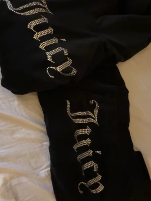 Svart Juicy Couture velourset - Säljer ett svart sett från Juicy Couture med glittrande strasstenar som stavar 'Juicy' på både byxben och tröja. Storlek S i tröjan, Xs i byxorna. Setet har dragkedja på tröjan och klassisk hoodie-stil. Perfekt för chill dagar hemma eller när du vill ha en ikonisk Y2K-look. Byxorna är uppsydda och sitter perfekt på mig som är 170💕