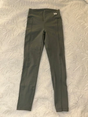 Grå/gröna träningstajts (XS) - Snygga grå/gröna träningstajts, med tight passform och stretchigt material. Har två fickor vid höfterna. Skriv vid frågor 🥰
