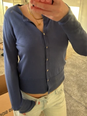 Mörkblå ribbad kofta med knappar - Snygg mörkblå kofta med långa ärmar och ribbade muddar. Koftan har en klassisk knappstängning framtill och är tillverkad i ett mjukt, tunt stickat material. Perfekt att styla med jeans eller kjol för en avslappnad look.