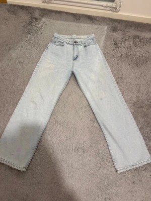 Ljusblå raka jeans med hög midja - Säljer ett par ljusblå jeans med raka ben och hög midja. Jeansen har klassisk femficksdesign och stängs med knapp och dragkedja. Perfekta för en avslappnad och trendig look. Tillverkade i jeansmaterial av bomull.