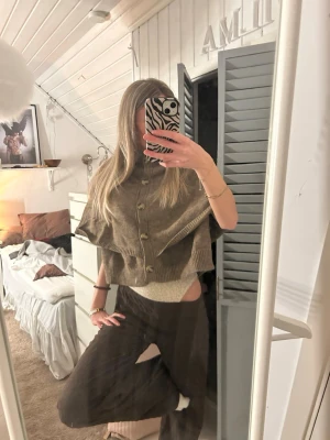 Beige stickad ponchotröja med knappar - Säljer en beige stickad ponchotröja med ribbade kanter och knäppning framtill. Tröjan har en lös, boxig passform och är perfekt att slänga över en topp för en chill look. Enkel och stilren design som passar till många outfits. aldrig använd