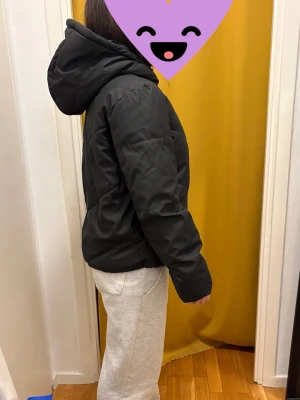 Svart pufferjacka med huva - Snygg svart pufferjacka med stor huva och quiltad design. Jackan har en klassisk passform och är perfekt för kyliga dagar. Nypris 399 säljer för 200kr, den är praktiskt taget oanvänd. Personen på bilden är runt 157 och väger 54kg. 