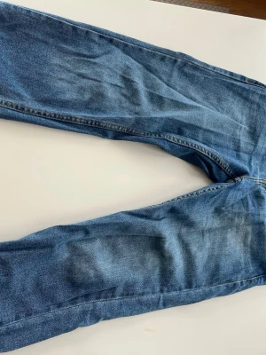 Levi's 501 blå jeans straight fit - Klassiska blå Levi's 501 jeans med rak passform och fem fickor. Jeansen har den ikoniska röda Levi's-lappen på bakfickan och är tillverkade i slitstarkt bomullsjeans. Perfekta för en avslappnad och tidlös stil.