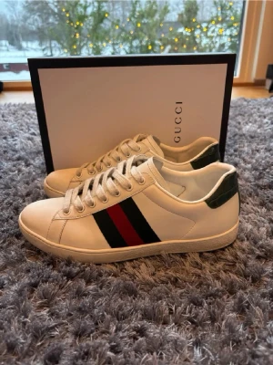 Gucci Ace -  Säljer mina vita Gucci Ace sneakers i storlek 42 med de klassiska röd-gröna ränderna på sidan. De passar till typ allt och ger riktigt clean fit 💯  Väldigt bra skick, använda några gånger men inget man tänker på! 📦 Medföljer: 	•	Original Gucci box 	•	Dustbag 	•	Kort/lappar (se bilder) Säljer pga kommer inte till användning, bara att skriva om de vill has fler bilder, snabb affär billigare pris👍