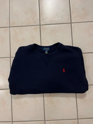 Mörkblå Polo Ralph Lauren tröja - Riktigt schysst mörkblå tröja från Polo Ralph Lauren med rund halsringning och röd logga utan luva. 