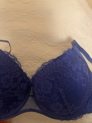 Blå spets- pushup bh från Hunkemöller - Snygg blå spets bh från Hunkemöller med vadderade kupor. Justerbara axelband och hakknäppning bak. Oanvänd!