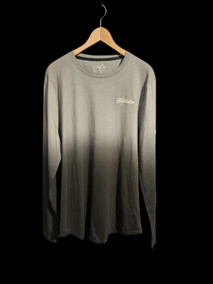 Grå ombre långärmad Hollistertröja stl XL mycket bra skick - Långärmad tröja från Hollister i grått ombre-mönster. Tröjan har rund halsringning och en liten vit Hollister-logga på bröstet. Tillverkad i 100% bomull.