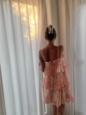 Rosa volangklänning med axelband - Söt kort klänning i ljusrosa toner med volanger och tunna axelband. Klänningen har ett lager-på-lager-utseende och ett lätt, luftigt tyg som passar perfekt för varma dagar✨💭🩷