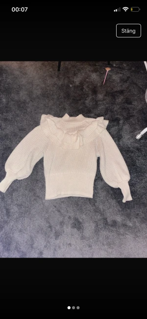 Beige stickad tröja med volang H&M - Superfin beige stickad tröja från H&M i storlek S. Tröjan har breda ribbade muddar, långärmade puffärmar och en snygg volangdetalj runt halsen som ger en extra touch. Perfekt för dig som gillar en söt och trendig stil.
