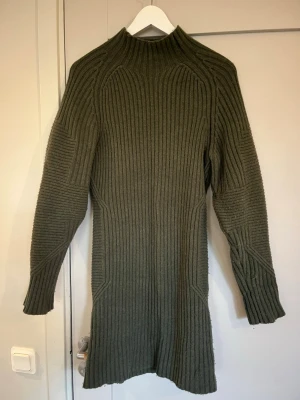 Olivgrön stickad tröja/klänning Twist & Tango - Säljer en olivgrön, ribbstickad polotröja från Twist & Tango i storlek M. Tröjan har lång ärm, hög krage och är tillverkad i en mjuk ull- och nylonmix. Snyggt strukturerad med markerade stickningar. 