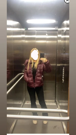 Vinröd pufferjacka med dragkedja - Säljer en vinröd pufferjacka med hög krage och dragkedja framtill. Jackan har en quiltad design och två sidofickor. Perfekt för kalla dagar och har en snygg, lite glansig finish. Passformen är normal och jackan är långärmad.