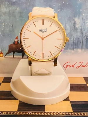 Snygg vit Damklocka  från Regal - Elegant Regal damklocka med en vit urtavla och guldfärgade detaljer. Klockan har ett quartz urverk och ett matchande vitt armband i läderimitation. Perfekt för den som söker en stilren och klassisk accessoar.Rustad med nytt batteri, säljes i befintligt fungerande skick enligt bilderna!