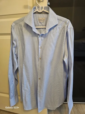 Blårutig skjorta från Michael Kors - Snygg blårutig skjorta från Michael Kors i modern fit. Skjortan har klassisk krage, långa ärmar och knappar framtill. Tillverkad i mjuk bomull som känns skön mot huden. Perfekt för dig som gillar stilrena och fräscha plagg med lite edge.
