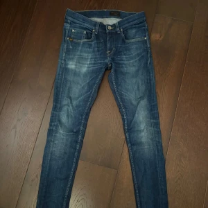 Blå skinny jeans från Tiger of Sweden - Snygga blå jeans från Tiger of Sweden med skinny passform och klassisk femficksdesign. Jeansen har en mörk tvätt med slitningar och är tillverkade i stretchig denim för en bekväm känsla. Perfekta för dig som gillar en smal siluett. OBS! Har ett snus märke på ena bak fickan