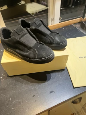 Svarta axel arigatos EU 45 - Snygga och stilrena slip-ons från Axel Arigato. Mjukt mockaläder, bra komfort och minimalistisk design. Använda men i gott skick (lite ytslitage på mockan) Originalbox och dust bag ingår.