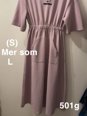 Ljuslila långklänning med huva - Ljuslila långklänning från Shein med huva, korta ärmar och resår i midjan. Klänningen har två stora fickor framtill som känns riktigt chill. Perfekt för dig som gillar avslappnad stil med coola detaljer.🌸 Fläckar. Kan finnas någon mer diffus än de på bilderna. Stor i storlek. Uppskattningsvis L ( står S)