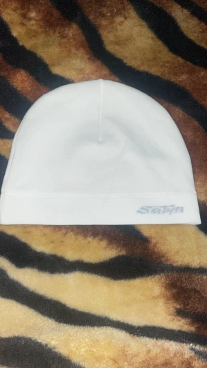 Vit satinmössa från Satyn - Snygg vit mössa från Satyn med slät utsida och glansig satin på insidan. Enkel och stilren design utan mönster, perfekt för att lyfta din outfit. Västen har en klassisk form och är tillverkad i mjukt material med satinlining för extra komfort.