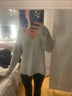 Grå stickad v-ringad tröja Vero Moda - Mysig grå stickad tröja från Vero Moda med v-ringning och lång ärm. Tröjan har en loose fit och är perfekt för lager-på-lager. Ribbstickad struktur och enkel design som funkar till allt.