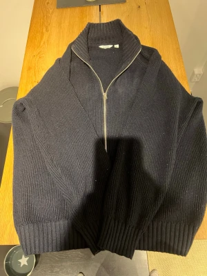 Svart stickad kofta från Dobber L - Svart ribbstickad kofta från Dobber i storlek L. Koftan har hög krage och hel dragkedja framtill. Tjockt och mjukt material som passar perfekt när det är kallt. Enkel och stilren design som funkar till många outfits.