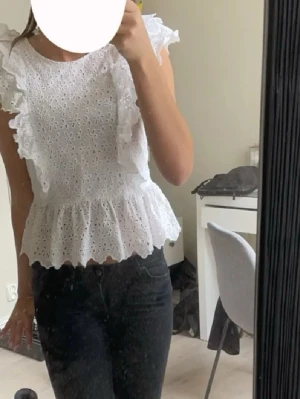 Vit blommig blus med volanger - Supersöt vit blus med broderade blommor och volangdetaljer längs axlarna. Kommer tyvärr inte till användning längre🥰 pris kan diskuteras. Storlek 42, men skulle säga den är som en Xs/S 