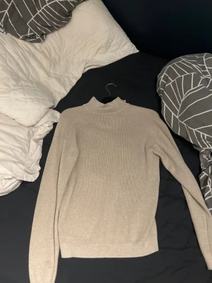 Beige stickad half zip polotröja - Snygg beige stickad polotröja med half zip-dragkedja i halsen. Tröjan har långärmad passform och är ribbad i materialet, vilket ger en schysst struktur. Perfekt för dig som gillar stilrena och neutrala färger. 158/164 storlek.