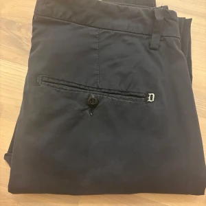 Mörkblå chinos från Dondup - Mörkblå chinos från Dondup, ett italienskt märke känt för sina välgjorda byxor. Klassisk modell med raka ben, bälteshällor och fickor fram samt bak med knapp. Storlek 33. Mått: midja 38 cm, längd 103 cm, benslut 14 cm, insida ben 25 cm.