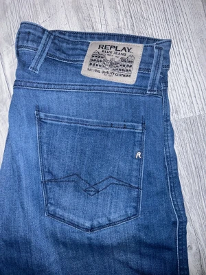 Replay Anbass slim fit jeans blå - Snygga blå Replay Anbass jeans i slim fit med klassisk femficksdesign och diskret Replay-logga på fickan. Jeansen har raka ben och är tillverkade i mjukt denimtyg som sitter skönt. Perfekta för dig som gillar stilrena och moderna jeans.
