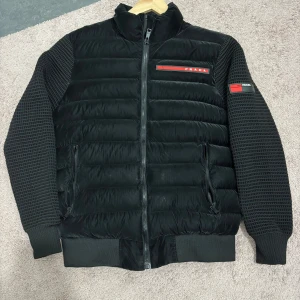 Svart pufferjacka  - Svart pufferjacka med quiltad kropp och stickade ärmar. Jackan har dragkedja framtill, ribbade muddar. Snygg, modern design som sticker ut med sin mix av material och detaljer. Qr koden finns även på.