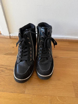 Svarta sneakers  - Svarta sneakers med 7 cm klack och gulddekor, gott skick.