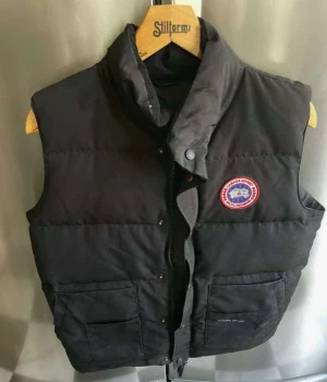 Canada goose väst  - Svarta canada goose väst med broderad logga på framsidan. Västen har flera fickor och en dubbel dragkedja, perfekt för kalla höstar.