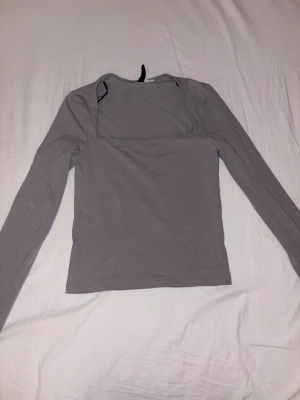Grå långärmad topp med fyrkantig hals - Säljer en stilren grå långärmad topp med en snygg fyrkantig halsringning. Toppen är enkel och har en normal passform, perfekt att matcha med jeans eller kjol. Materialet känns mjukt och bekvämt mot huden.