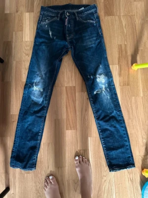 Dsquared2 blå skinny jeans, strl 46 - Snygga blå jeans från Dsquared2 i storlek 46 med slitna detaljer och distressed look. Modellen är skinny med normal passform och klassisk femficksdesign. Jeansen är tillverkade i bomull och har en mörk tvätt med coola slitningar på benen. Som nya, använda fåtal gånger.