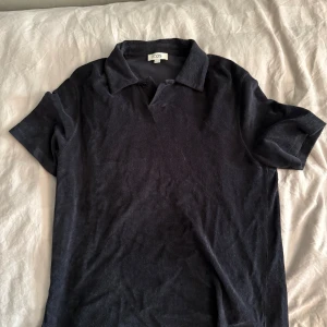 Svart pikétröja i frotté från COS - Svart pikétröja från COS i storlek L, tillverkad i mjuk frotté. Klassisk krage och korta ärmar ger en clean och chill look. Perfekt för dig som gillar minimalistisk stil och vill ha något bekvämt och snyggt.