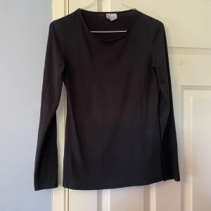 Svart långärmad topp från Divided - En svart, enkel långärmad topp från Divided. Modellen har rund halsringning och är figurnära i passformen. Perfekt att styla med jeans eller kjol för en clean look. Tillverkad i mjuk bomull som känns skön mot huden.