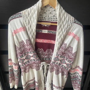 Mönstrad odd molly kofta med knyt  - Superfin kofta i beige med vinröda, svarta och rosa mönster. Koftan har virkade detaljer vid kragen, knytband i midjan och långa ärmar. Perfekt för lager-på-lager och ger en mysig boho-vibe till din outfit.