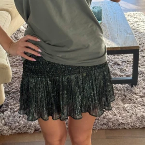 Glittrig svart minikjol med volang - Supersnygg svart glittrig minikjol med plisserad volangkant. Kjolen har resår i midjan och hade även inbyggda shorts som jag har klippt isär så de endast är en kjol med innertyg, inget som syns!💕