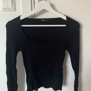 Svart ribbad topp från Gina Tricot - Svart långärmad topp från Gina Tricot med ribbad struktur och snygg fyrkantig ringning. Modellen är figurnära och stretchig, perfekt att styla med jeans eller kjol. Enkel och stilren design som funkar året runt.