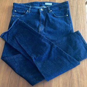 Mörkblå jeans från Tiger of Sweden - Snygga mörkblå jeans från Tiger of Sweden med klassisk femficksdesign och raka ben. Jeansen har orange kontrastsömmar, silverfärgad knapp och patch med logga bak i midjan. Tillverkade i slitstarkt denimtyg av bomull. W32 L30.