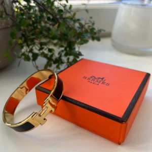 Svart och guld armband  - Stilrent armband i svart och guld med click H-detaljen framtill. Armbandet har en elegant, rundad form. 