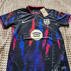 FC Barcelona x Nike blood and colors - Snygg FC Barcelona matchtröja från Nike i svart med färgstarka röda och blå penseldrag, Spotify-logga på bröstet och klubbmärke. Kortärmad modell i lätt och ventilerande Dri-FIT-material. Unik design med detaljer och tryck inspirerade av konst och sport.