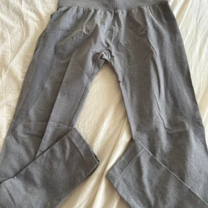 Grå leggings från NVGTN - Snygga grå leggings från NVGTN med hög midja och bred ribbad linning. Materialet är stretchigt och mjukt, perfekt för träning eller chill. Diskreta mörkare detaljer på baksidan ger extra stilpoäng. Supersköna och sitter riktigt bra!