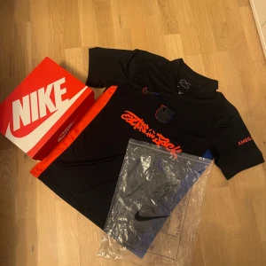 Nike x FC Barcelona Cactus Jack tröja - Snygg svart fotbollströja från Nike i samarbete med FC Barcelona och Cactus Jack. Tröjan har korta ärmar, röda och blå detaljer samt grafiskt tryck på bröstet. Materialet är lätt och andas, perfekt för match eller träning.